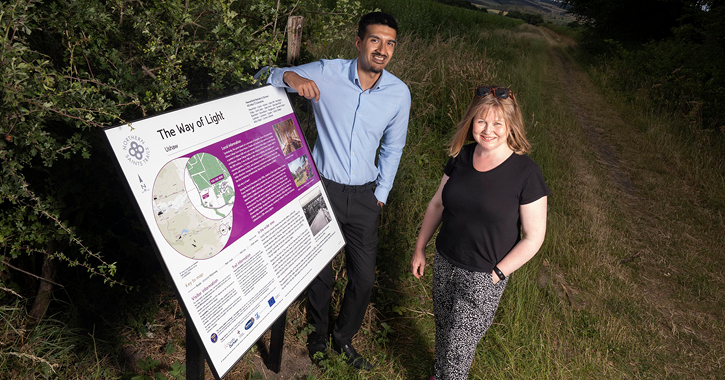 Cllr Elizabeth Scott and Sanjay Gidda stand next to Northern Saints Trails interpretation panel.